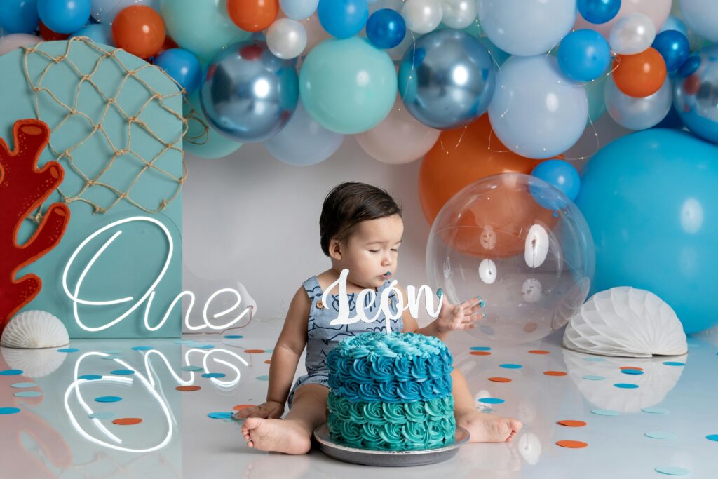 Adorable baby enjoying first birthday cake smash with colorful balloons.